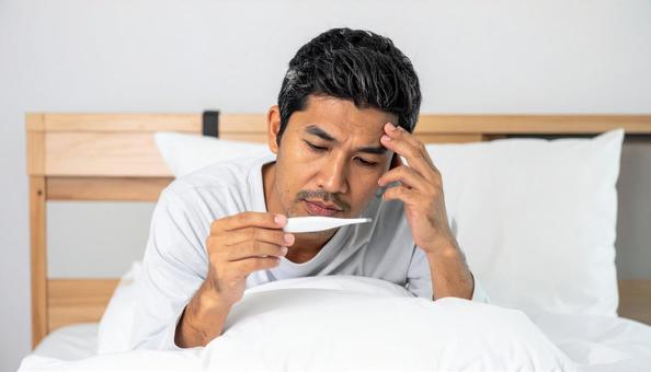 寝ながら体温計で熱を測る日本人男性 寝ながら体温計で熱を測る日本人男性の写真