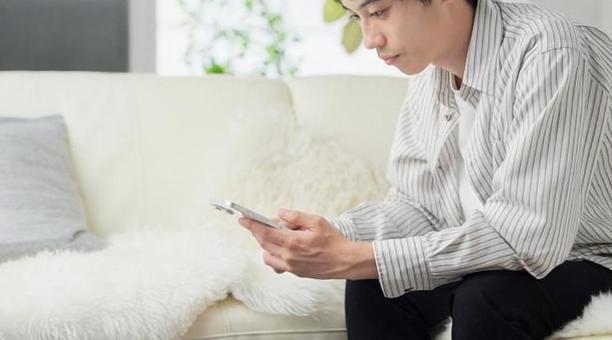 リビングでスマートフォンを見る男性 男性,スマホ,スマートフォンの写真素材