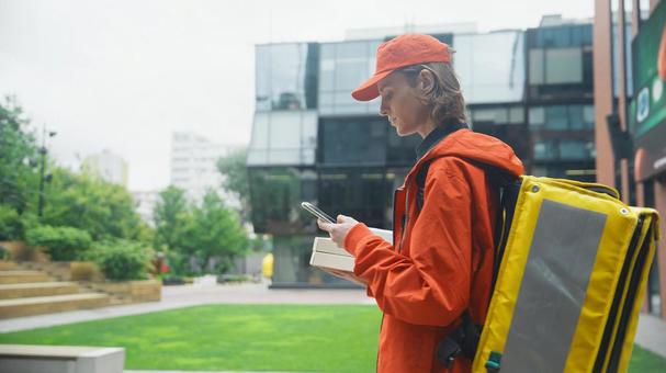 ピザ箱を持ってスマートフォンを使っているフードデリバリーの男性 配達,フードデリバリー,デリバリーの写真素材