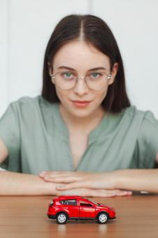 模型の車を前に笑顔を浮かべる女性 保険業,事務職,接客業の写真素材
