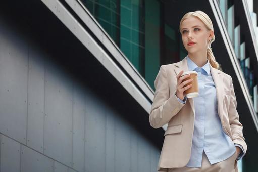 オフィスビルの外に居るコーヒーを持った外国人ビジネスウーマン ビジネスウーマン,ビジネス,女性の写真素材