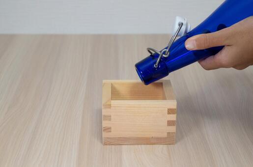 青いガラス瓶から枡に液体を注ぐ手元 枡,青い,瓶の写真素材