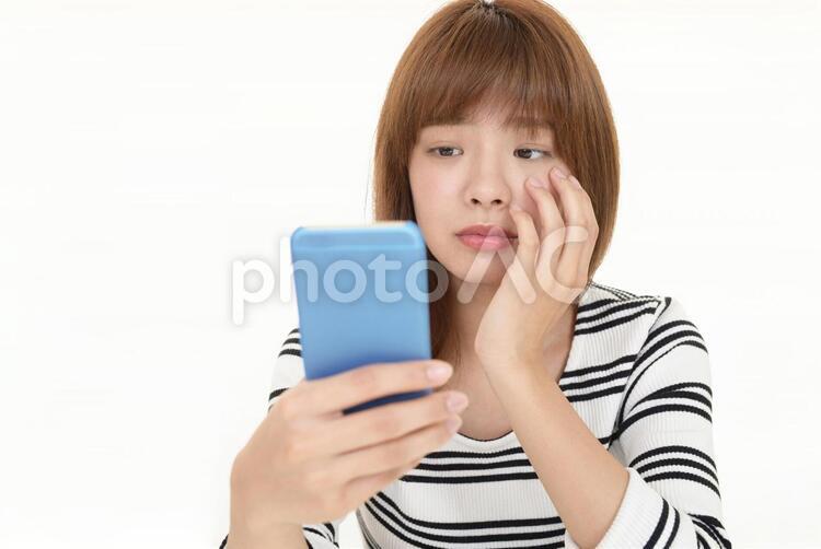 スマートフォンを持つ悲しそうな表情の女性 女性,スマートフォン,携帯電話の写真素材