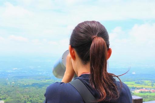 山頂の展望台から双眼鏡で景色を見る女性 山頂の展望台から双眼鏡で景色を見る女性の写真