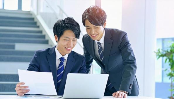 パソコンと資料を見ながら相談する社員 パソコンと資料を見ながら相談する社員の写真