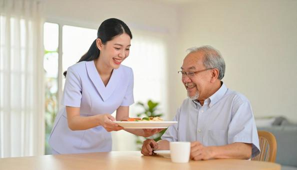 笑顔で食事を運ぶ女性介護士と高齢男性 笑顔で食事を運ぶ女性介護士と高齢男性の写真