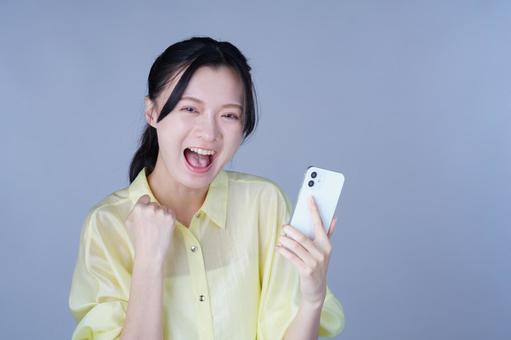 スマホでガッツポーズ、黄色い服の女性の写真