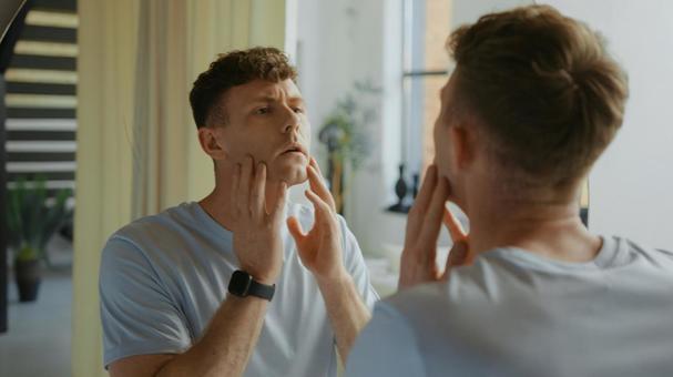 鏡を見ながら両手で頬を触る男性 男性,外国人,欧米人の写真素材