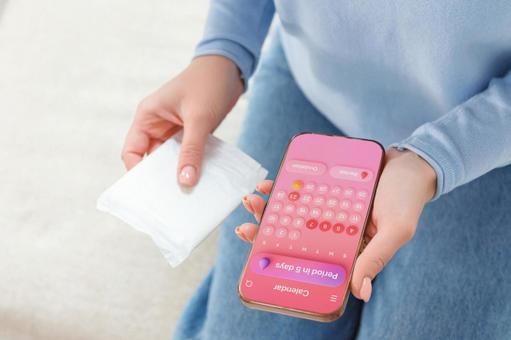 生理用ナプキンと生理周期アプリを立ち上げたスマートフォンを持っている女性 生理,月経,女性の写真素材