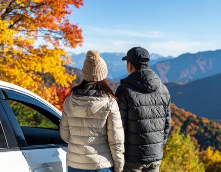 紅葉の山々を眺めるカップルの秋ドライブ 紅葉の山々を眺めるカップルの秋ドライブの写真