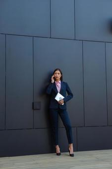 オフィスビルの黒い壁の前で電話しているアジア人女性 ビジネスウーマン,ビジネス,女性の写真素材