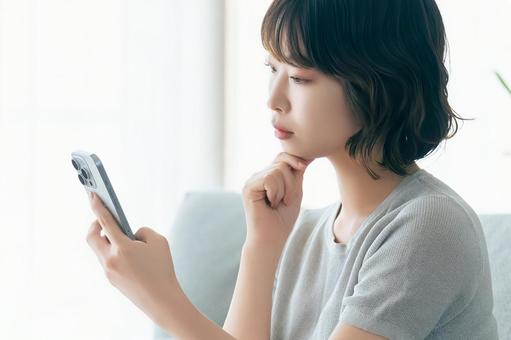 A woman thinking while looking at her smartphone, JPG