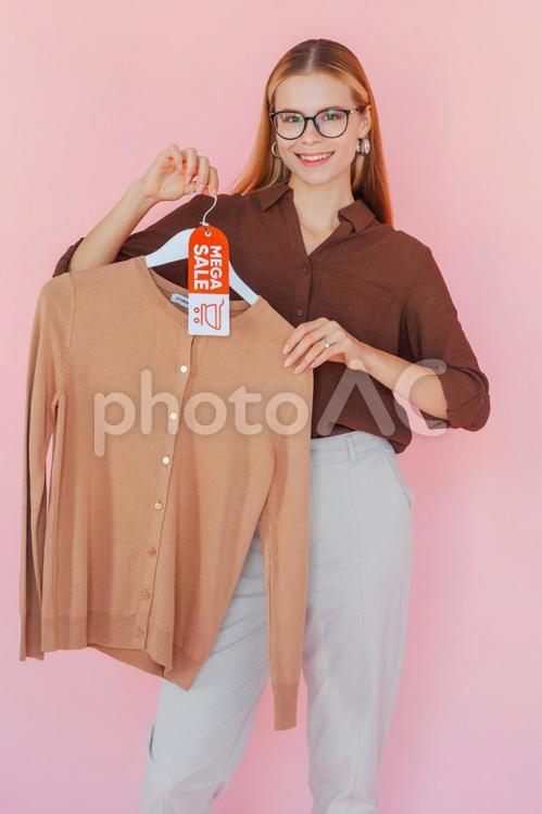 セールのタグの付いたハンガーに掛かった洋服を持っているカメラ目線で笑顔の女性 セール,ショップ,女性の写真素材