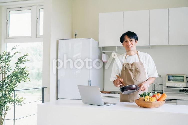 パソコンを見ながら料理する男性（笑顔） 料理,家事,パソコンの写真素材