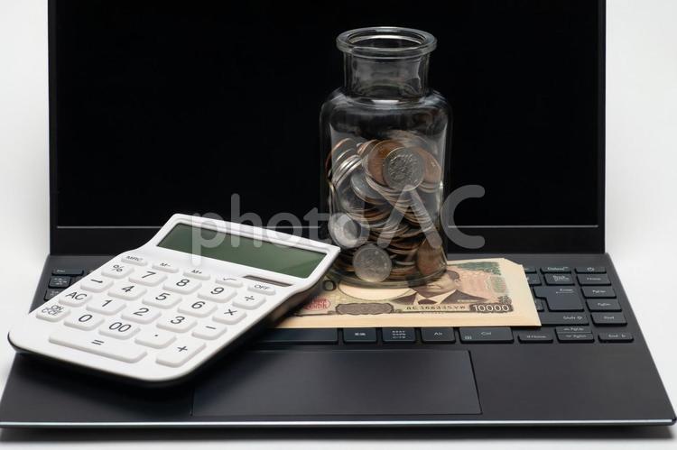 ノートパソコンと広口瓶に入った小銭と紙幣 お金,パソコン,電卓の写真素材