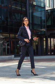 オフィス街をスマートフォン片手に歩くビジネスウーマン ビジネスウーマン,ビジネス,女性の写真素材