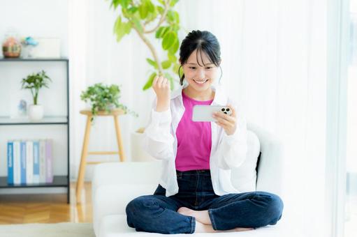 部屋でスマホを操作する若い女性 スマホ,笑顔,若い女性の写真素材