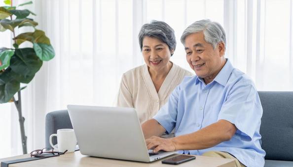 リビングで仲良くパソコンを見るシニア夫婦の写真