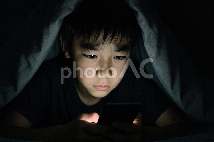 布団を被りスマホを操作する男の子 ai生成,人物,男の子の写真素材