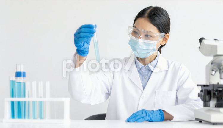 研究所で実験をする女性の研究者 試薬,フラスコ,マスクの写真素材
