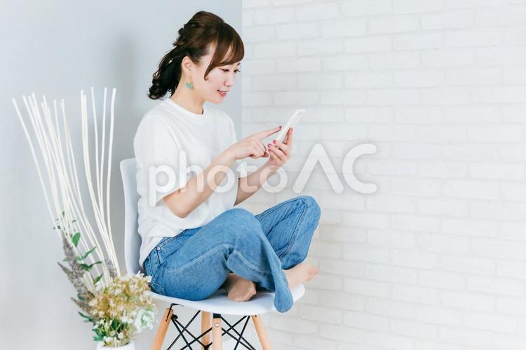 椅子に座りながら笑顔でスマホを使う女性 スマホ,女性,スマートフォンの写真素材