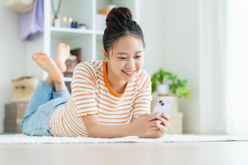 リビングでスマホを使う若い女性 リビングでスマホを使う若い女性の写真