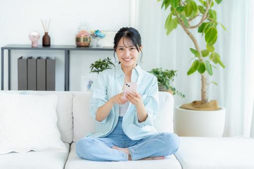 部屋でスマホを操作する若い女性 スマホ,笑顔,女性の写真素材