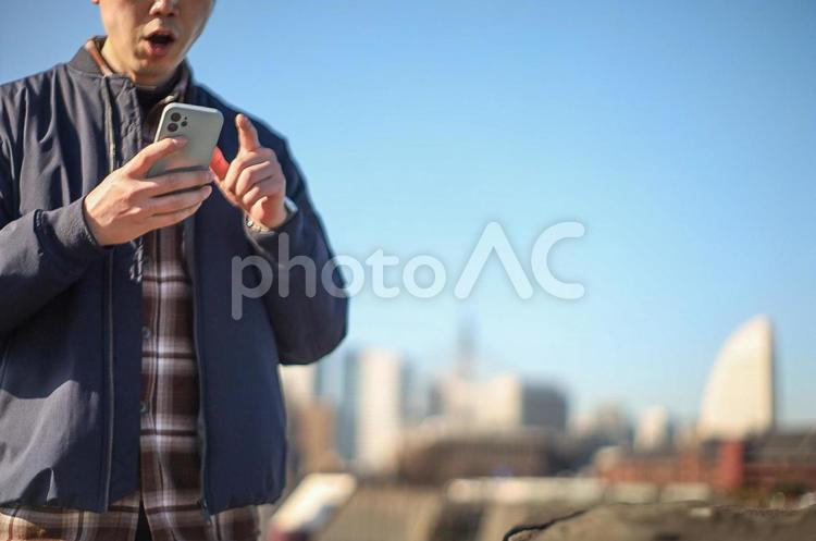 外でスマホを操作する男性 驚き,びっくり,スマホの写真素材