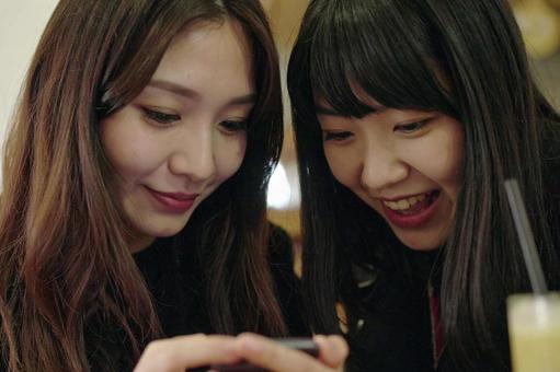 スマホを見ながら会話を楽しむ女子大生 スマホを見ながら会話を楽しむ女子大生の写真