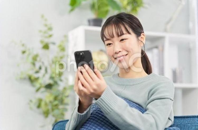ソファに座ってスマートフォンを見る女性 女性,スマートフォン,ソファの写真素材