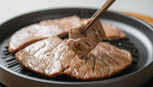 焼肉を鉄板で焼いて箸ですくうの写真