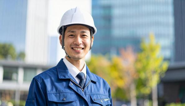 高層ビル前で笑顔のヘルメット作業服の男性 高層ビル前で笑顔のヘルメット作業服の男性の写真