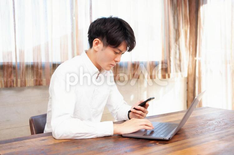 ノートパソコンとスマホを使う男性 テレワーク,スマホ,リモートワークの写真素材