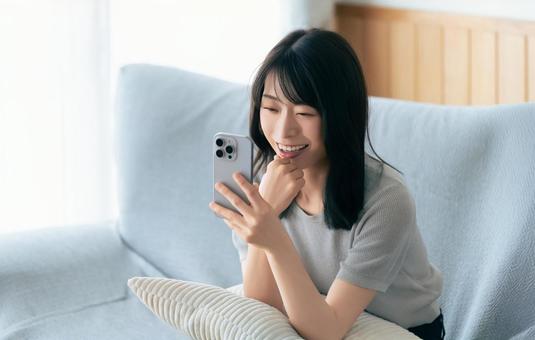 ソファに座ってスマホを使う笑顔の女性 ソファに座ってスマホを使う笑顔の女性の写真
