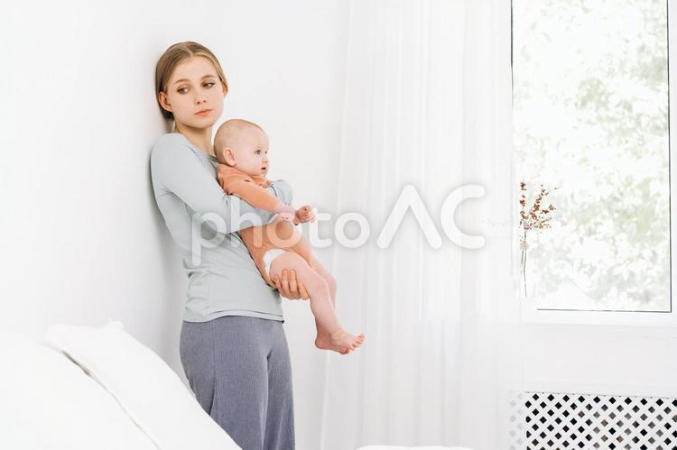 壁に寄り掛かり赤ちゃんを抱く疲れた顔の女性 女性,赤ちゃん,かわいいの写真素材