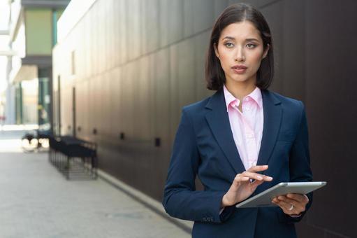 街なかでタブレットを使っているスーツの女性 ビジネスウーマン,ビジネス,女性の写真素材