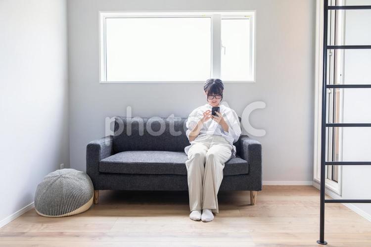 ソファーでスマホを操作する女性 スマホ,リラックス,女性の写真素材