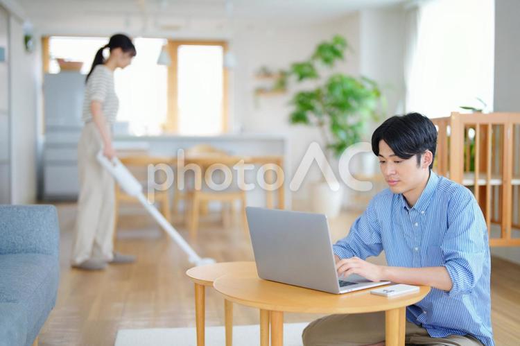 パソコンをする男性と掃除中の女性 男性,ノートパソコン,テレワークの写真素材