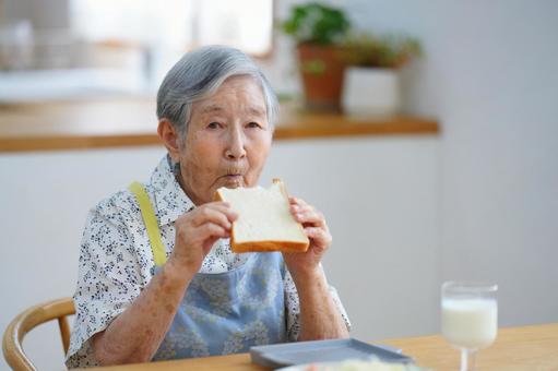 カメラ目線でパンを食べているおばあちゃん 女性,食パン,食べるの写真素材