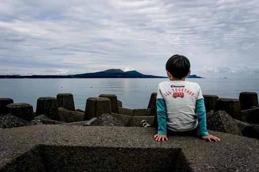 ＜素材＞防波堤の先きに座り海を見る男の子 子供,海,鬼岳の写真素材
