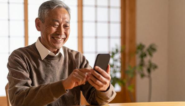 スマホを操作し笑顔の高齢日本人男性の室内 スマホを操作し笑顔の高齢日本人男性の室内の写真