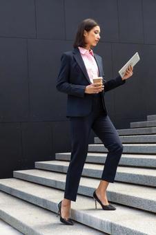 タブレットを見ながらオフィスビルの外の階段を登るビジネスウーマン ビジネスウーマン,ビジネス,女性の写真素材