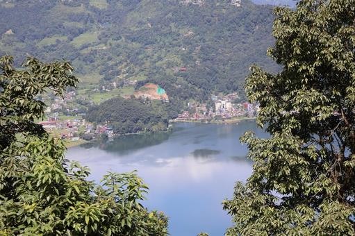 緑の木々の先に湖とポカラの街と山の風景 緑の木々の先に湖とポカラの街と山の風景の写真