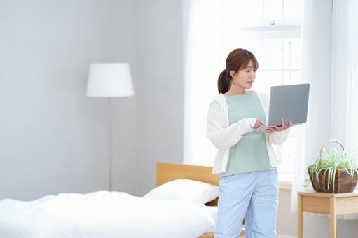 ベッドの横に立ちパソコン作業する女性 女性,ノートパソコン,持つの写真素材