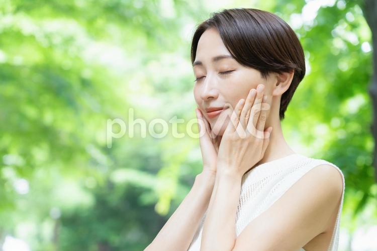 新緑の中でスキンケアをするミドルの女性 ビューティー,女性,スキンケアの写真素材