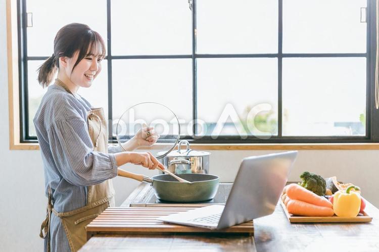 パソコンで動画を見ながら料理をする女性 料理,パソコン,レシピ動画の写真素材