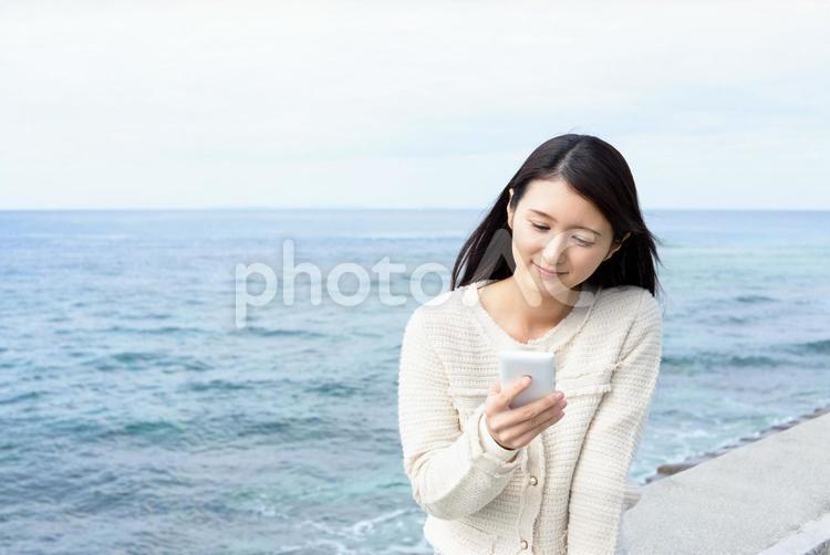海辺でスマートフォンを持つ女性 女性,スマホ,スマートフォンの写真素材