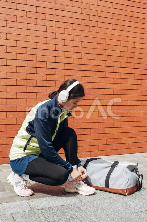 しゃがんで靴ひもを結ぶ女性とバッグ 女性,ヘッドフォン,横顔の写真素材