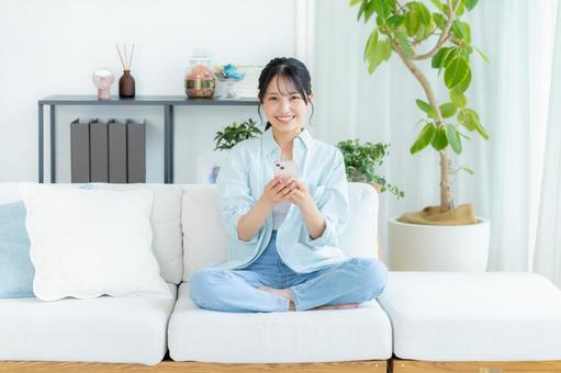 部屋でスマホを操作する若い女性 スマホ,笑顔,女性の写真素材