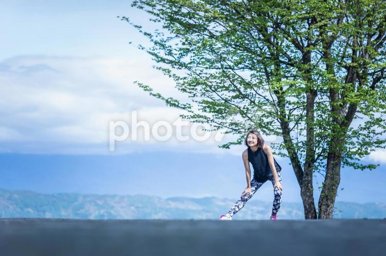 絶景の中にいるスポーツウェアの女性（屈伸・笑顔） 準備運動,背景,ウォーミングアップの写真素材